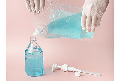 Hände mit Handschuhen füllen blaues Alkoholgel in Plastikflasche auf.