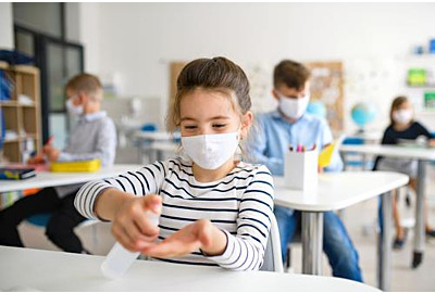 Hygienekonzept in Schulen: Kleines Mädchen mit Gesichtsmaske in der Schule nach Covid-19 Absperrung, Desinfektion der Hände.